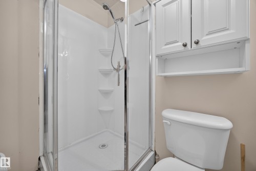 White shower enclosure with a clear glass door, built-in shelving, and a handheld showerhead - 8310 99 Avenue, Fort Saskatchewan, AB - Indoor Photo Showing Bathroom