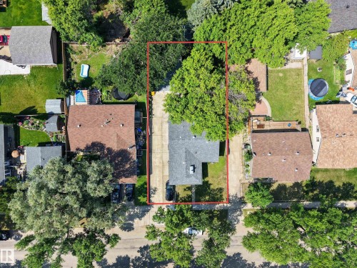 Aerial view of a residential property with a brown-roofed home, featuring a long driveway, a grassy backyard, and mature trees providing shade - 8310 99 Avenue, Fort Saskatchewan, AB - Outdoor With View