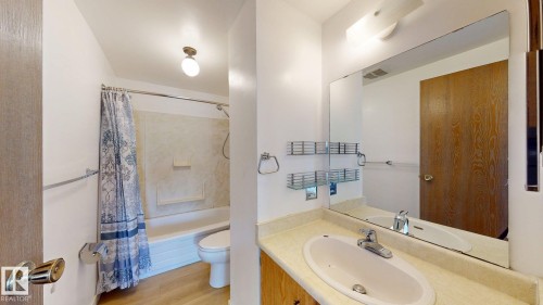 Bathroom featuring a single vanity with an integrated sink, a large mirror, a combined shower and tub, and wood-finish flooring - 4912 34A Avenue, Edmonton, AB - Indoor Photo Showing Bathroom