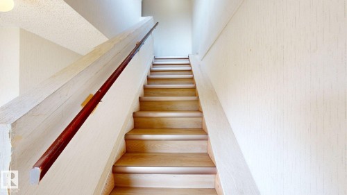 Staircase with light wood-finish treads and risers, featuring a dark wood-finish handrail and textured wall finishes - 4912 34A Avenue, Edmonton, AB - Indoor Photo Showing Other Room