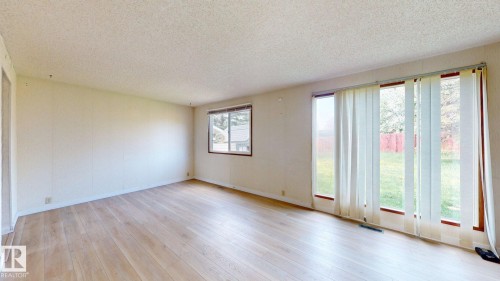 Spacious interior room featuring wood-finish flooring, light-toned walls, and a textured ceiling - 4912 34A Avenue, Edmonton, AB - Indoor