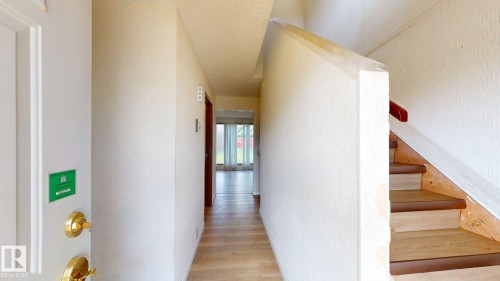Entryway featuring wood-finish flooring extending into the hallway, a staircase with a red-toned handrail, and a white entrance door with brass hardware - 4912 34A Avenue, Edmonton, AB - Indoor Photo Showing Other Room