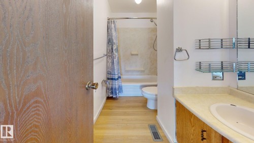 Bathroom featuring a white toilet, built-in bathtub with shower, wood-finish flooring, and a vanity with an integrated sink and light-toned countertop - 4912 34A Avenue, Edmonton, AB - Indoor Photo Showing Bathroom