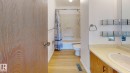 Bathroom featuring a white toilet, built-in bathtub with shower, wood-finish flooring, and a vanity with an integrated sink and light-toned countertop - 4912 34A Avenue, Edmonton, AB  - Indoor Photo Showing Bathroom 