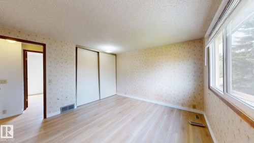 Spacious room featuring light wood-finish flooring, patterned wallpaper, and a large window with white blinds - 4912 34A Avenue, Edmonton, AB - Indoor Photo Showing Other Room