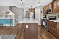 Kitchen featuring a central island with an undermount sink, white countertops, stainless steel appliances, and wood-finish flooring - 