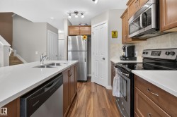 Kitchen featuring wood-finish flooring, white countertops, stainless steel appliances, a double basin sink, and a tile backsplash - 