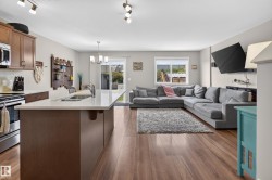 Open-concept living area featuring wood-finish flooring, a kitchen island with an undermount sink, stainless steel appliances, and a sliding glass door to the exterior - 