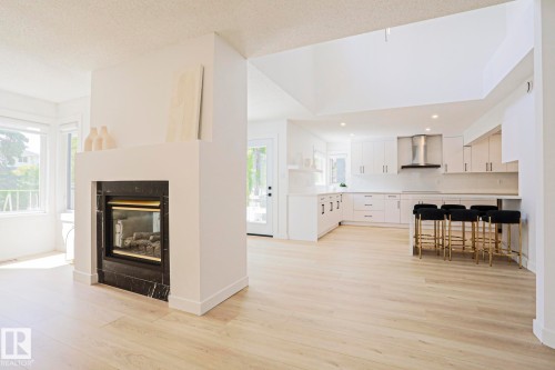 Open-concept living space featuring light wood-finish flooring, a contemporary fireplace with a dark stone surround, and an expansive kitchen - 11347 10 Avenue, Edmonton, AB - Indoor With Fireplace