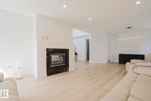 Living area featuring a fireplace with a black marbled surround, light wood-finish flooring, recessed lighting, and a modern linear pendant fixture - 11347 10 Avenue, Edmonton, AB - Indoor Photo Showing Living Room With Fireplace