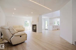 Spacious living area featuring light wood-finish flooring, a contemporary fireplace with a white surround, recessed lighting, a modern linear light fixture, and an abundance of natural light from the bay window - 