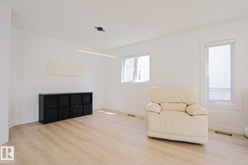 Spacious room featuring light wood-finish flooring, white painted walls, and multiple windows - 11347 10 Avenue, Edmonton, AB - Indoor Photo Showing Living Room