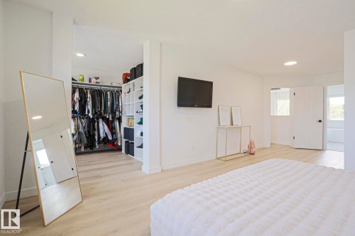 Spacious bedroom featuring light wood-finish flooring, recessed lighting, a built-in open closet system with shelving and hanging rods, and a white paneled door - 11347 10 Avenue, Edmonton, AB - Indoor Photo Showing Bedroom