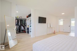 Spacious bedroom featuring light wood-finish flooring, recessed lighting, a built-in open closet system with shelving and hanging rods, and a white paneled door - 