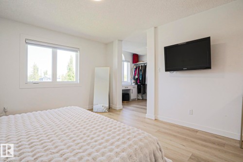 Spacious bedroom featuring light wood-finish flooring, a large window, a wall-mounted television, and a recessed area with built-in cabinetry and clothing storage - 11347 10 Avenue, Edmonton, AB - Indoor Photo Showing Bedroom