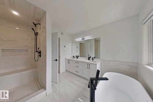 Spacious bathroom featuring a freestanding tub, a walk-in shower with bench seating and a niche, a double vanity with ample storage, a large mirror, and light-toned tile flooring - 11347 10 Avenue, Edmonton, AB - Indoor Photo Showing Bathroom