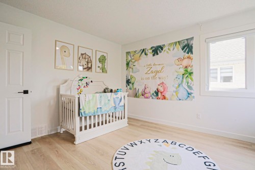 Bright room featuring light wood-finish flooring, white painted walls, a white paneled door with black hardware, and a large window - 11347 10 Avenue, Edmonton, AB - Indoor