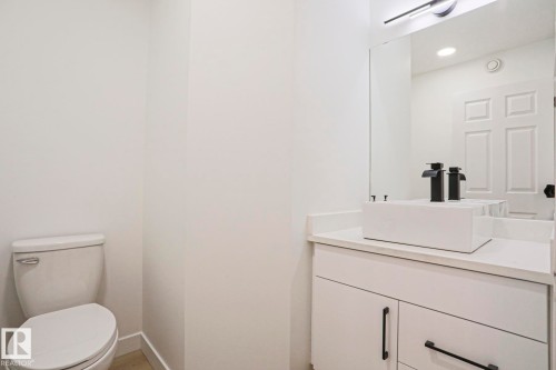 Powder room featuring a white vessel sink with matte black fixtures, a coordinating white vanity with black hardware, and a large wall-mounted mirror - 11347 10 Avenue, Edmonton, AB - Indoor