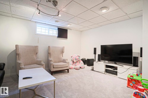 Carpeted recreation room featuring white painted walls, a grid panel ceiling with track lighting, and a window with security bars - 11347 10 Avenue, Edmonton, AB - Indoor Photo Showing Other Room
