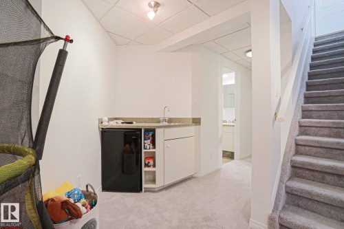 Lower level entertainment area featuring a wet bar with a compact refrigerator, built-in cabinetry, and a stone countertop - 11347 10 Avenue, Edmonton, AB - Indoor Photo Showing Bedroom