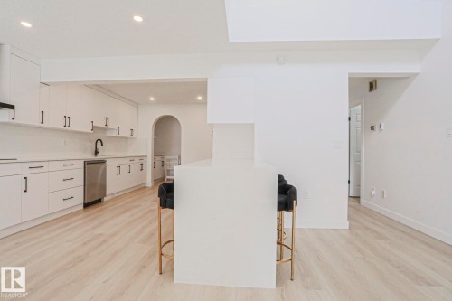 Modern kitchen featuring white cabinetry, stainless steel dishwasher, black faucet, and light wood-finish flooring - 11347 10 Avenue, Edmonton, AB - Indoor Photo Showing Kitchen