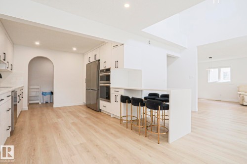 Renovated kitchen featuring a large island with counter seating, stainless steel appliances including a refrigerator and double oven, white cabinetry with black hardware, and wood-finish flooring - 11347 10 Avenue, Edmonton, AB - Indoor Photo Showing Kitchen