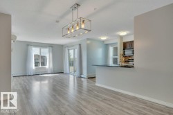 Open-concept living area featuring wood-finish flooring, a modern linear chandelier, and light-colored walls - 