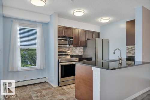 Kitchen featuring dark wood-finish cabinetry, stainless steel appliances and a breakfast bar. - #201 534 Watt Bv Sw, Edmonton, AB - Indoor Photo Showing Kitchen With Upgraded Kitchen