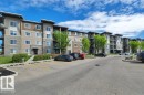 Multi-story residential building featuring a stone and siding exterior, multiple balconies, and a paved parking area with designated spaces - #201 534 Watt Bv Sw, Edmonton, AB  - Outdoor With Facade 