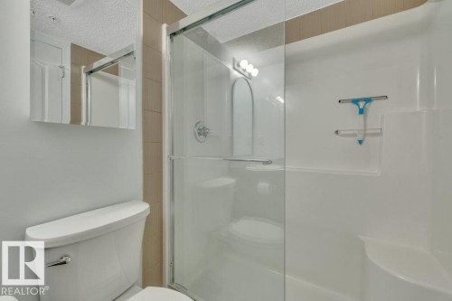 Shower stall with glass enclosure, white molded shower surround, tiled wall accent, and chrome fixtures - #201 534 Watt Bv Sw, Edmonton, AB - Indoor Photo Showing Bathroom