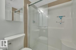 Shower stall with glass enclosure, white molded shower surround, tiled wall accent, and chrome fixtures - 