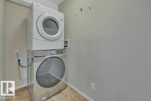 Dedicated laundry area featuring a stacked washer and dryer - #201 534 Watt Bv Sw, Edmonton, AB - Indoor Photo Showing Laundry Room