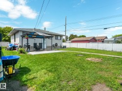 Expansive rear yard featuring a concrete patio with an attached awning, stucco exterior siding, and a white chain-link fence - 