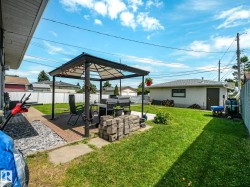 Spacious backyard featuring a covered patio structure, expansive green lawn, and a detached auxiliary building - 