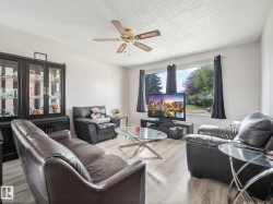 Living area featuring light wood-finish flooring, white walls, and a ceiling fan with integrated lighting - 