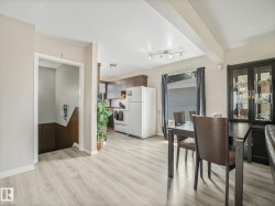 Open-concept living space featuring wood-finish flooring, a kitchen with dark cabinetry and white appliances, and a dining area with track lighting - 