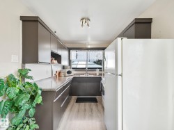 Galley kitchen featuring dark wood-finish cabinetry, light wood-finish flooring, a white refrigerator, a double basin sink, and ample countertop space - 