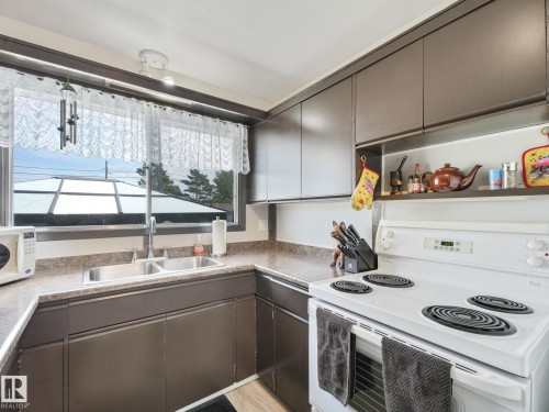 Kitchen featuring dark wood-finish cabinetry, a double basin stainless steel sink, and speckled laminate countertops - 13323 58 Street Nw, Edmonton, AB - Indoor Photo Showing Kitchen With Double Sink