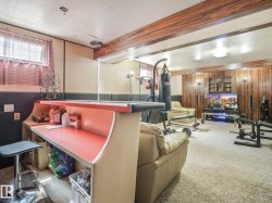 Recreation room featuring wood-finish accent wall paneling, built-in shelving, recessed ceiling lighting, and a built-in bar with a red countertop - 