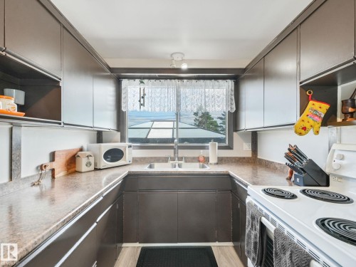 U-shaped kitchen featuring wood-finish cabinetry, a window with exterior scenery, a dual-basin sink, and a white electric range - 13323 58 Street Nw, Edmonton, AB - Indoor Photo Showing Kitchen With Double Sink