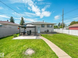 Expansive backyard featuring a manicured lawn, a concrete patio with a permanent gazebo, and a paved pathway - 