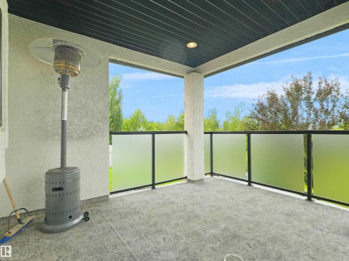 Covered outdoor patio featuring a textured concrete floor, frosted glass panel railing with dark framing, and a dark paneled ceiling with recessed lighting - 3136 35 Avenue Nw, Edmonton, AB - Outdoor With Exterior