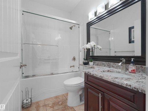 Full bathroom featuring a white tub with clear glass sliding doors, a rich wood-tone vanity with a light-toned stone countertop, a rectangular undermount sink, and a framed mirror with overhead vanity lighting - 3136 35 Avenue Nw, Edmonton, AB - Indoor Photo Showing Bathroom