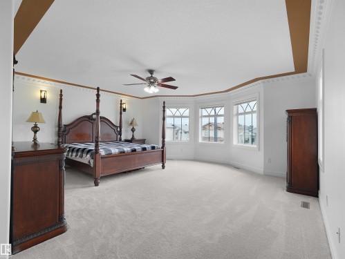 Spacious bedroom featuring light-toned carpeting, a tray ceiling with accent paint, ornate crown molding, and a ceiling fan with integrated lighting - 3136 35 Avenue Nw, Edmonton, AB - Indoor Photo Showing Bedroom