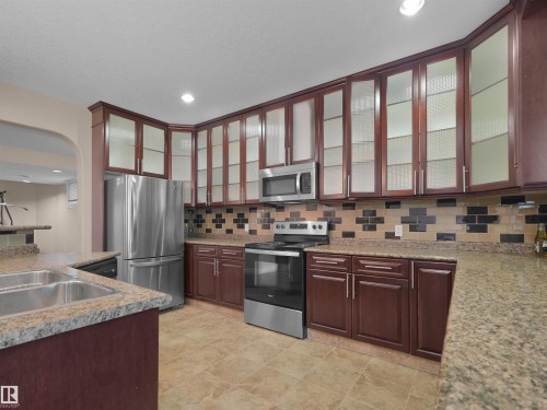 Kitchen featuring wood-finish cabinetry, stainless steel appliances, granite countertops, and a patterned tile backsplash - 3136 35 Avenue Nw, Edmonton, AB - Indoor Photo Showing Kitchen With Double Sink