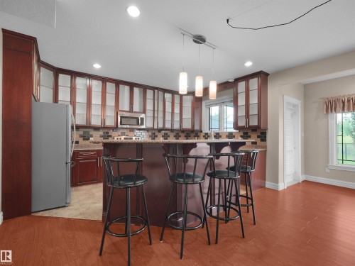 Kitchen featuring wood-finish cabinetry with glass panel doors, stainless steel appliances, granite countertops, and a tile backsplash - 3136 35 Avenue Nw, Edmonton, AB - Indoor