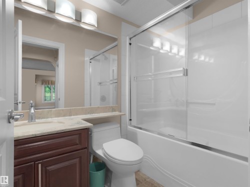 Bathroom featuring a full vanity with a dark wood-finish cabinet and a light-toned countertop, a mirror with a three-light fixture, and a shower-tub combination with a sliding glass door - 3136 35 Avenue Nw, Edmonton, AB - Indoor Photo Showing Bathroom
