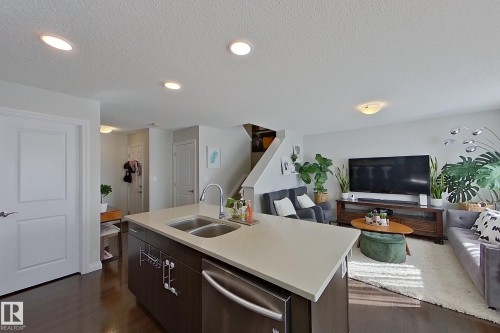 Open-concept living space with dark wood-finish flooring, recessed ceiling lighting, and a kitchen island featuring an undermount double sink and stainless steel dishwasher - 491 Ebbers Way, Edmonton, AB 