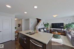 Open-concept living space with dark wood-finish flooring, recessed ceiling lighting, and a kitchen island featuring an undermount double sink and stainless steel dishwasher - 