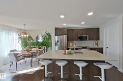 Open-concept kitchen and dining area featuring a large center island with seating, stainless steel appliances, dark wood-finish cabinetry, and recessed lighting - 